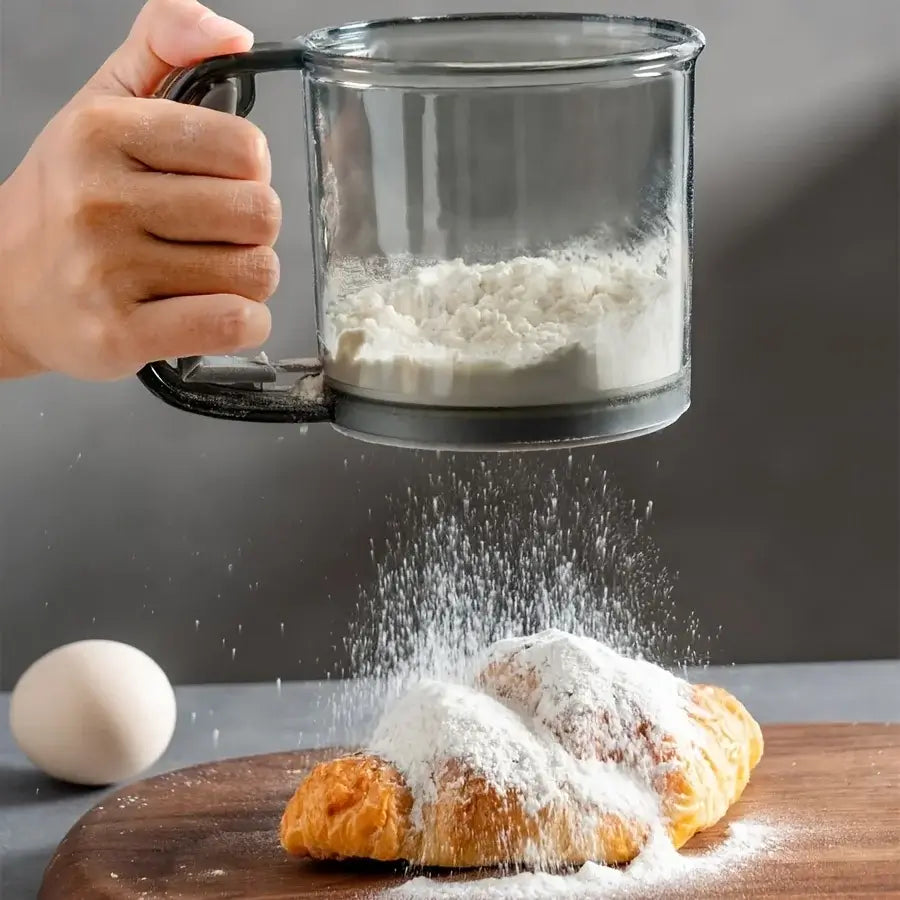 Hand sprinkling powdered sugar over pastries on a wooden board with a glass container of sugar.