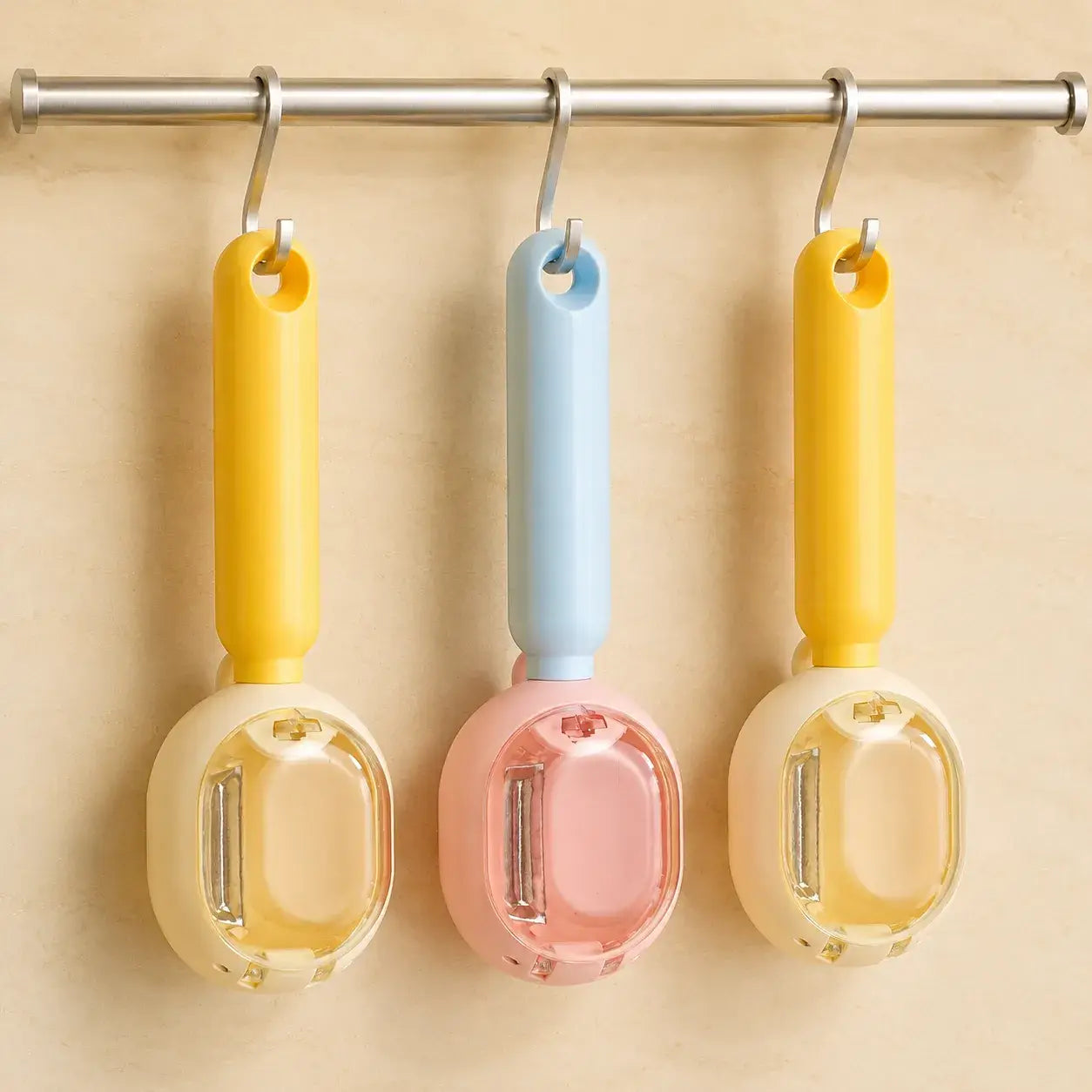 Three pastel PeelCatch peelers hanging on a kitchen rail
